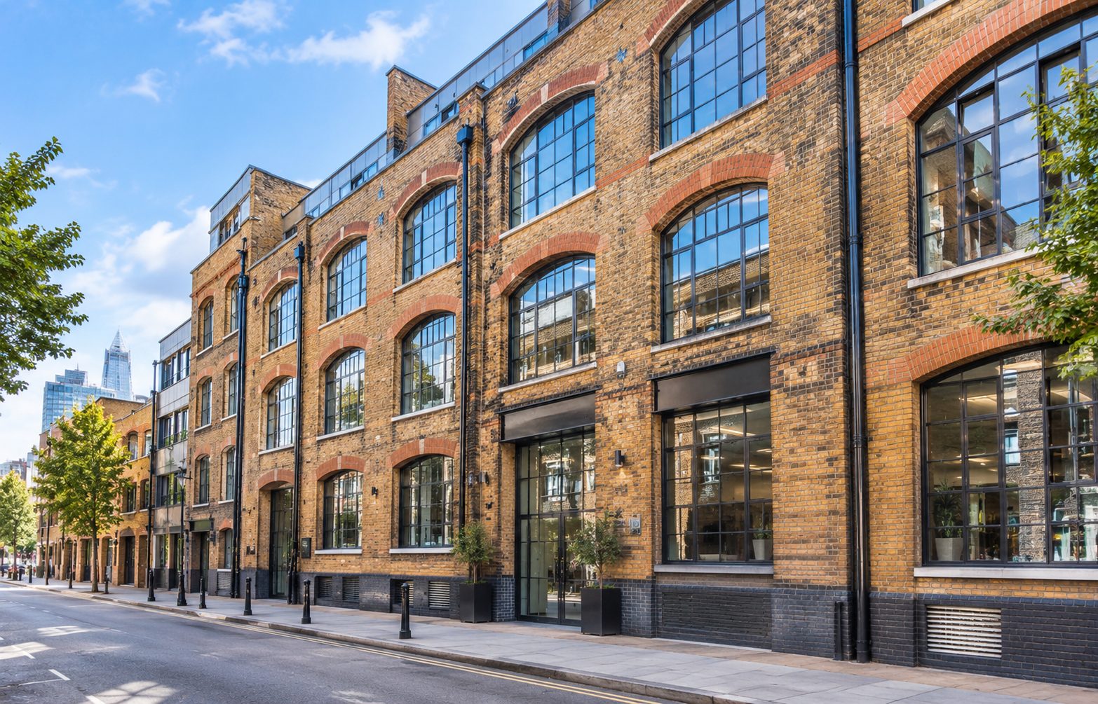 Exterior of a brick-fronted Victorian warehouse conversion in Clerkenwell or Shoreditch with large arched windows, shot from street level in daylight. 